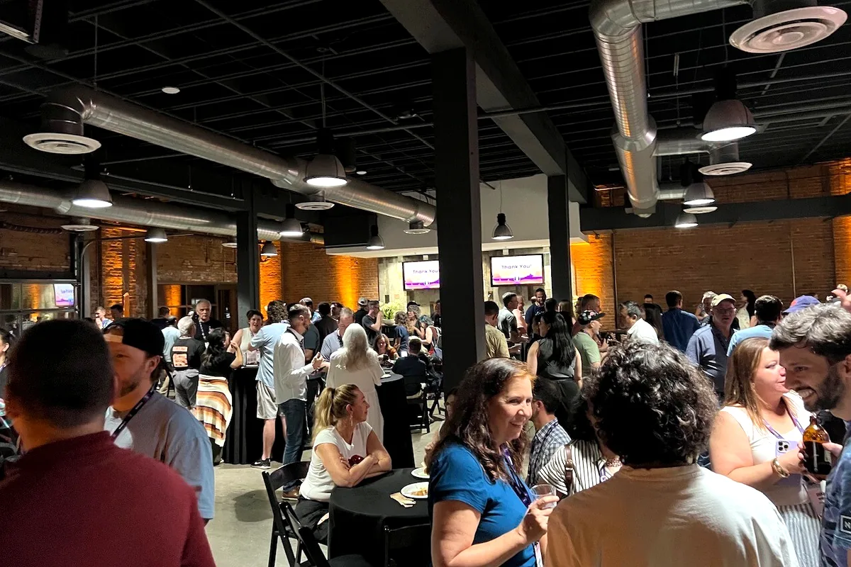 A busy room of WordCamp US attendees talking during an evening community party.